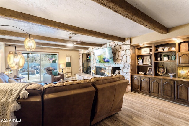 living room featuring a textured ceiling, beam ceiling, light hardwood / wood-style floors, and a fireplace