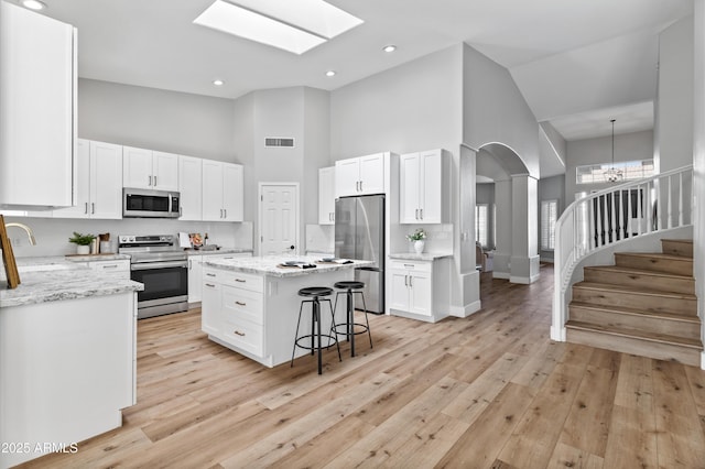 kitchen featuring a high ceiling, white cabinets, stainless steel appliances, and a kitchen island