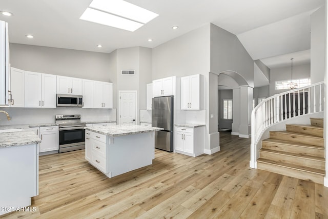 kitchen with appliances with stainless steel finishes, a center island, white cabinetry, high vaulted ceiling, and light stone counters