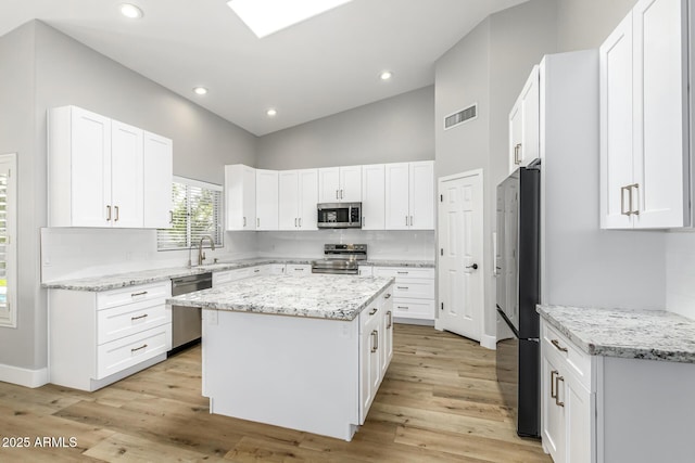 kitchen with appliances with stainless steel finishes, sink, white cabinets, a center island, and high vaulted ceiling