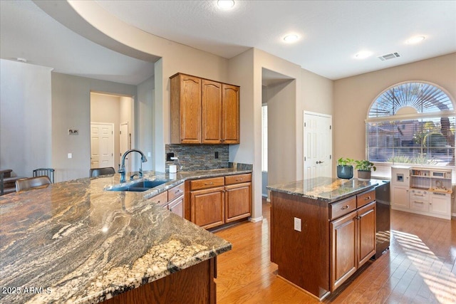 kitchen with light wood-style flooring, a sink, visible vents, brown cabinets, and dark stone countertops