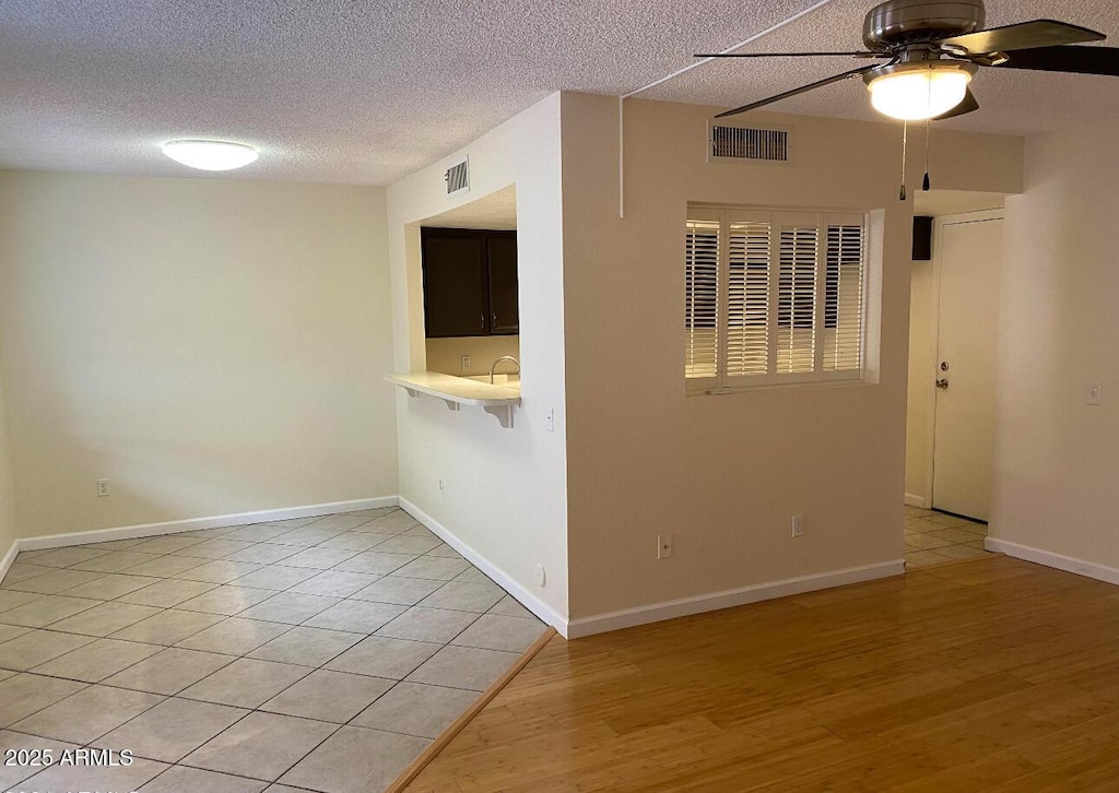 spare room with ceiling fan, light wood finished floors, a textured ceiling, and baseboards