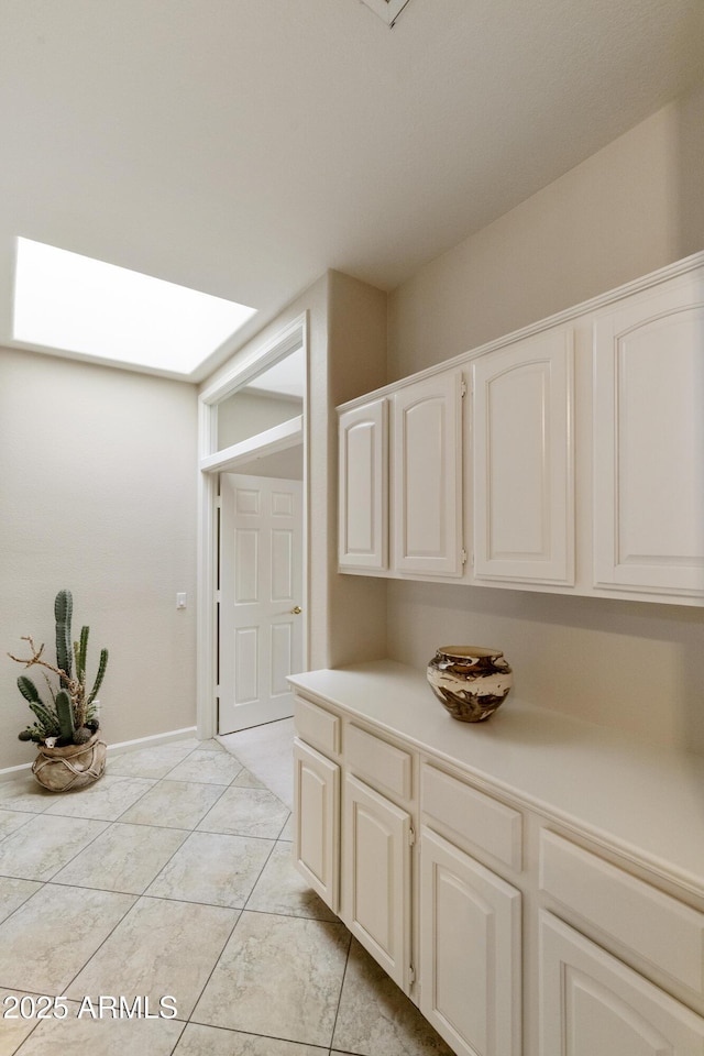 interior space with white cabinetry, light tile patterned floors, and a skylight