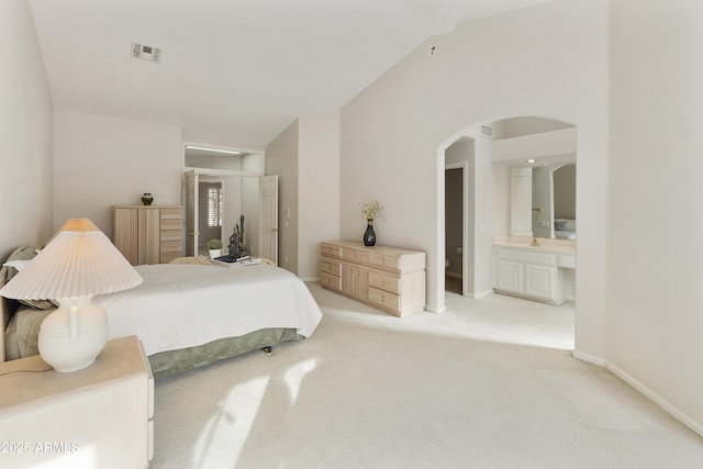 bedroom featuring ensuite bath, light carpet, and vaulted ceiling