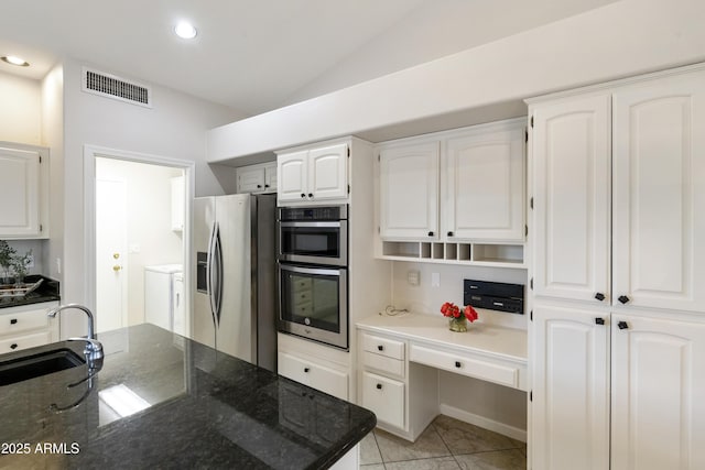 kitchen with dark stone counters, stainless steel appliances, vaulted ceiling, sink, and white cabinets