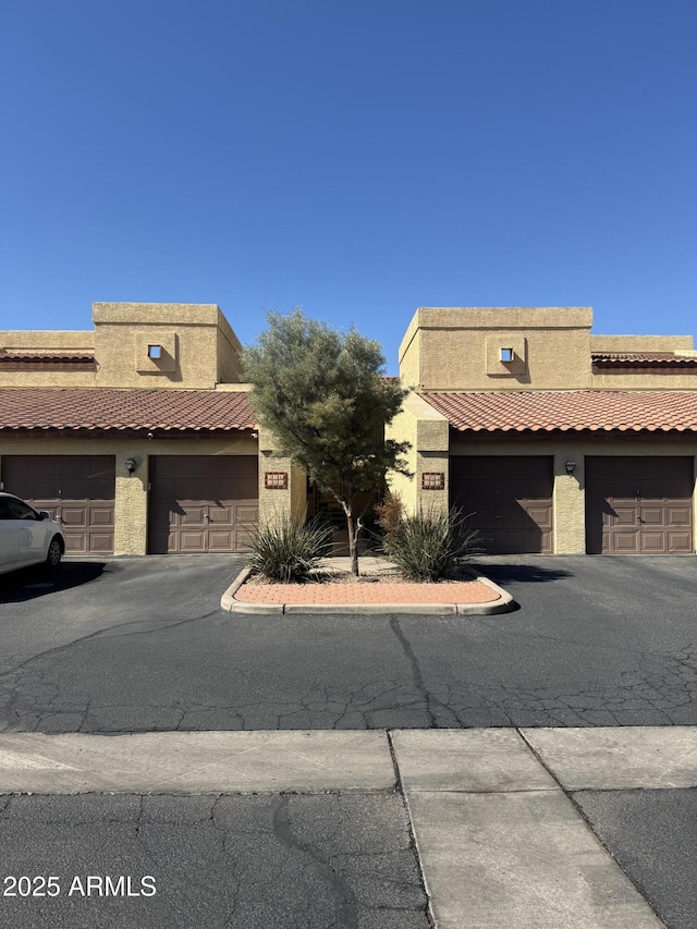 view of property featuring community garages, stucco siding, and a tile roof