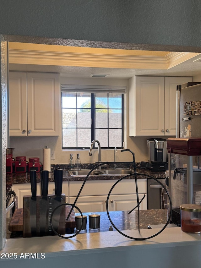 kitchen with dark countertops, visible vents, crown molding, white cabinets, and a sink