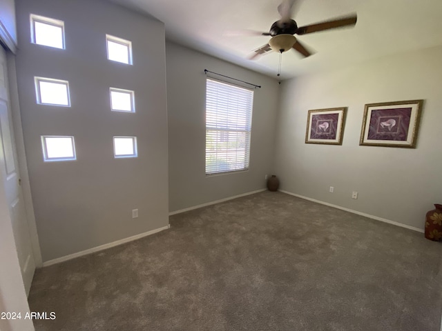 spare room with a ceiling fan, baseboards, and dark carpet