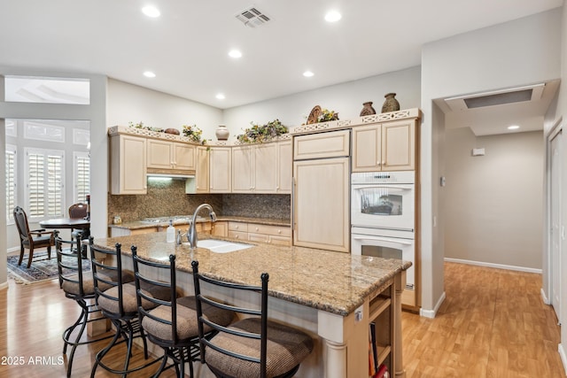 kitchen featuring double oven, light wood-type flooring, tasteful backsplash, and a sink