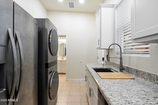 12943 W Mclellan Rd, Glendale, AZ 85307 - clothes washing area featuring a sink, cabinet space, light tile patterned floors, stacked washer and clothes dryer, and visible vents