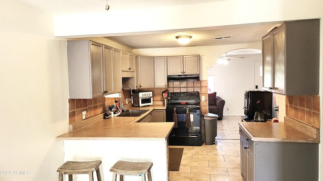 kitchen with decorative backsplash, gray cabinetry, black range with electric stovetop, a breakfast bar, and sink