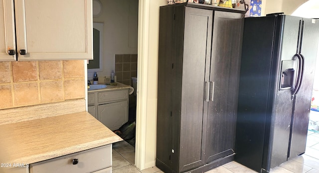 kitchen with backsplash, black fridge with ice dispenser, sink, and light tile patterned floors