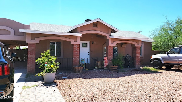 view of front of house featuring covered porch, a shingled roof, brick siding, and stucco siding