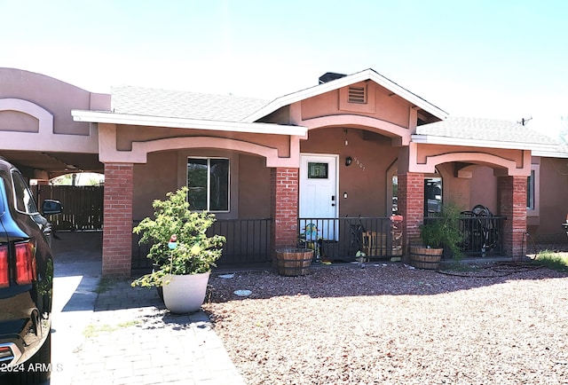 view of front facade featuring covered porch, roof with shingles, and stucco siding