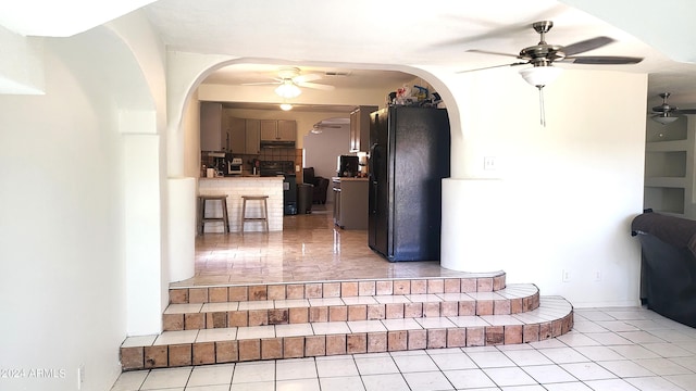 interior space featuring light tile patterned floors, arched walkways, freestanding refrigerator, ceiling fan, and stove