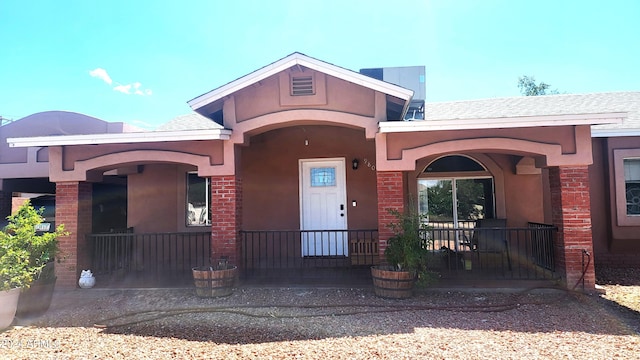 property entrance with stucco siding, covered porch, and a shingled roof