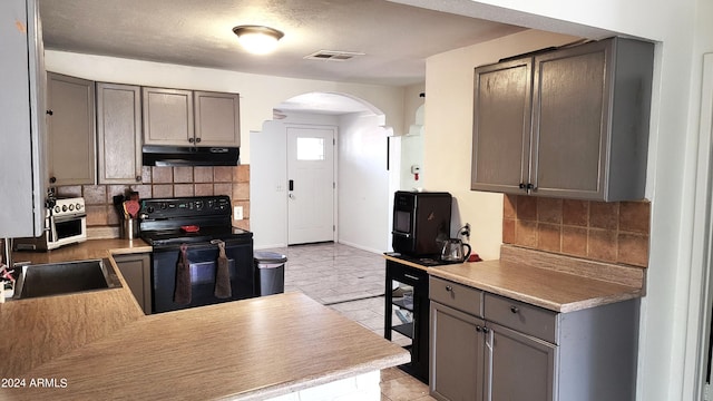 kitchen with visible vents, black range with electric cooktop, under cabinet range hood, gray cabinets, and arched walkways