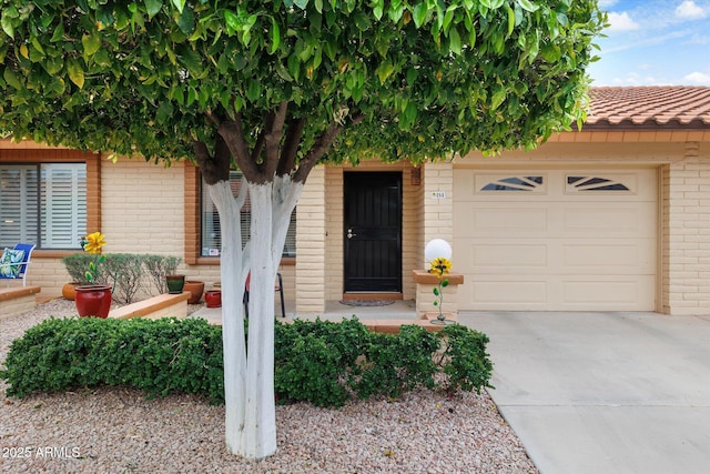 property entrance with a garage, brick siding, driveway, and a tiled roof