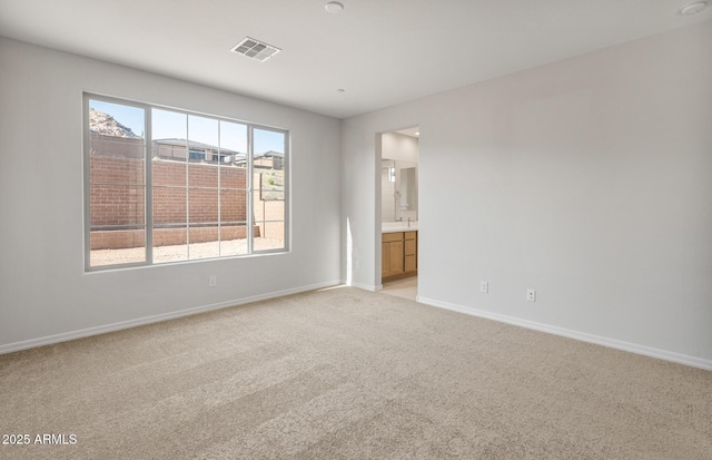 unfurnished bedroom featuring light colored carpet, connected bathroom, baseboards, and visible vents