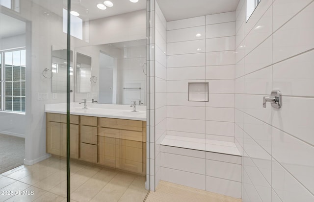 full bath featuring double vanity, a tile shower, a sink, tile patterned floors, and baseboards