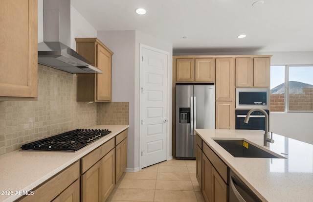 kitchen featuring wall chimney range hood, appliances with stainless steel finishes, tasteful backsplash, light stone countertops, and a sink