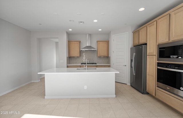 kitchen with wall chimney range hood, appliances with stainless steel finishes, light countertops, an island with sink, and recessed lighting