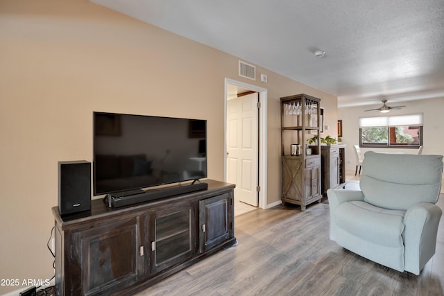 living room featuring a ceiling fan, baseboards, wood finished floors, visible vents, and a textured ceiling