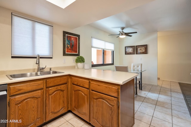 kitchen featuring light tile patterned floors, a peninsula, a sink, light countertops, and brown cabinets