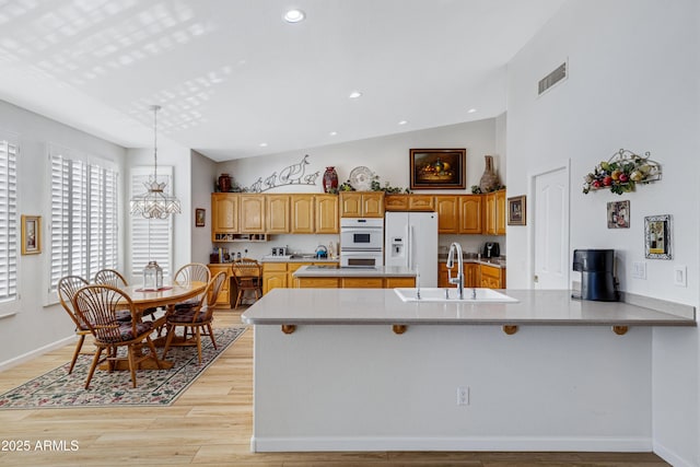 kitchen with sink, light hardwood / wood-style flooring, a chandelier, vaulted ceiling, and white appliances