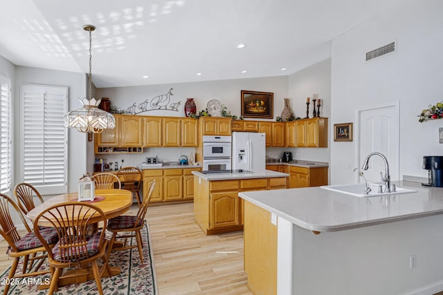 kitchen featuring pendant lighting, a center island, white appliances, sink, and light hardwood / wood-style flooring