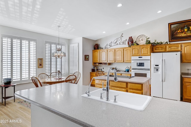 kitchen with white appliances, sink, light hardwood / wood-style flooring, an inviting chandelier, and hanging light fixtures