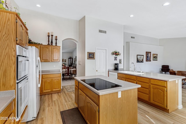 kitchen with sink, light hardwood / wood-style flooring, kitchen peninsula, white appliances, and a kitchen island