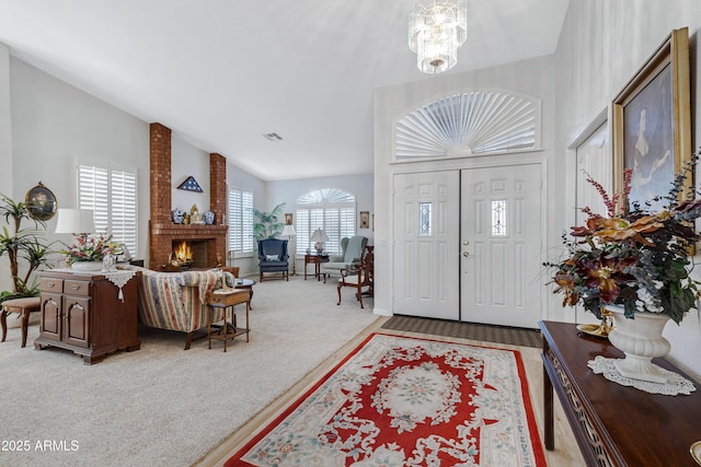 carpeted entrance foyer featuring a fireplace, plenty of natural light, high vaulted ceiling, and a notable chandelier