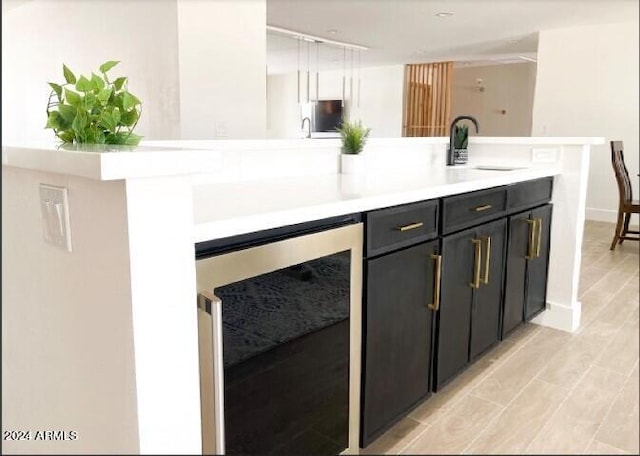 bar featuring sink, beverage cooler, and light wood-type flooring