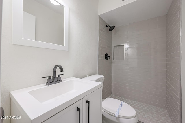 bathroom with tiled shower, vanity, and toilet