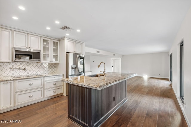 kitchen featuring sink, light stone counters, appliances with stainless steel finishes, dark hardwood / wood-style flooring, and an island with sink