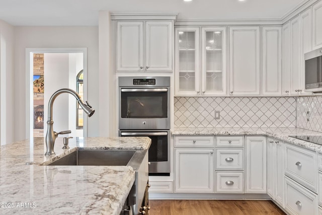 kitchen featuring sink, tasteful backsplash, light stone counters, stainless steel appliances, and white cabinets