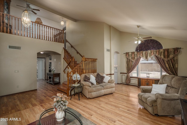 living area featuring ceiling fan, visible vents, arched walkways, high vaulted ceiling, and stairs