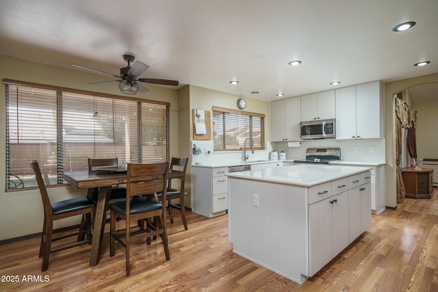 kitchen featuring white cabinets, appliances with stainless steel finishes, a sink, light countertops, and a kitchen island
