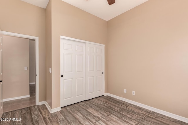 unfurnished bedroom with ceiling fan, baseboards, a closet, and wood finished floors