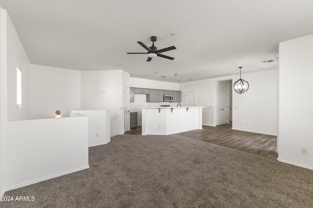 unfurnished living room featuring ceiling fan with notable chandelier and dark carpet