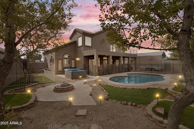 back house at dusk featuring a pool with hot tub, a patio, an outdoor fire pit, and a balcony