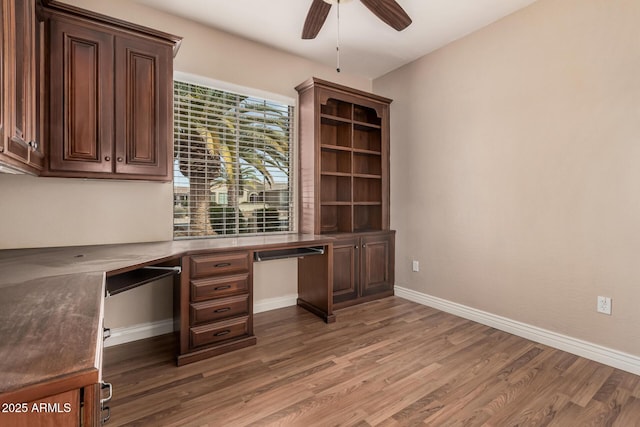 unfurnished office with wood-type flooring, built in desk, and ceiling fan