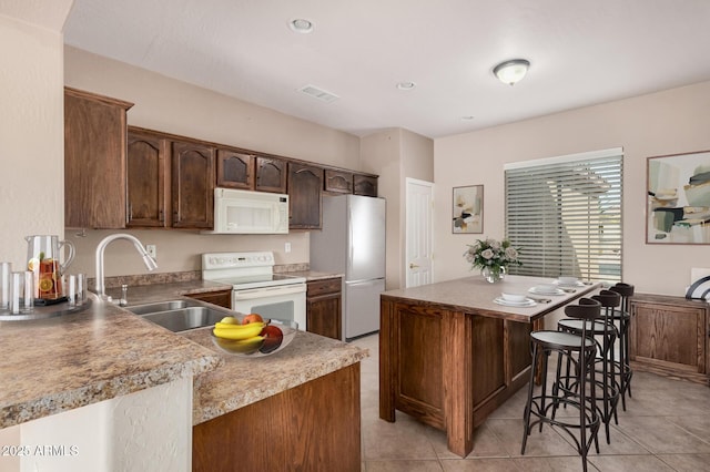 kitchen with a breakfast bar, sink, a center island, dark brown cabinets, and white appliances