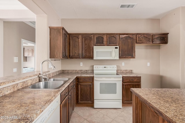 kitchen featuring dark brown cabinetry, sink, white appliances, and light tile patterned floors