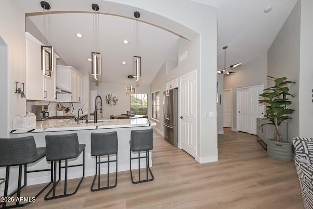 kitchen with high end fridge, hanging light fixtures, kitchen peninsula, light hardwood / wood-style floors, and white cabinets