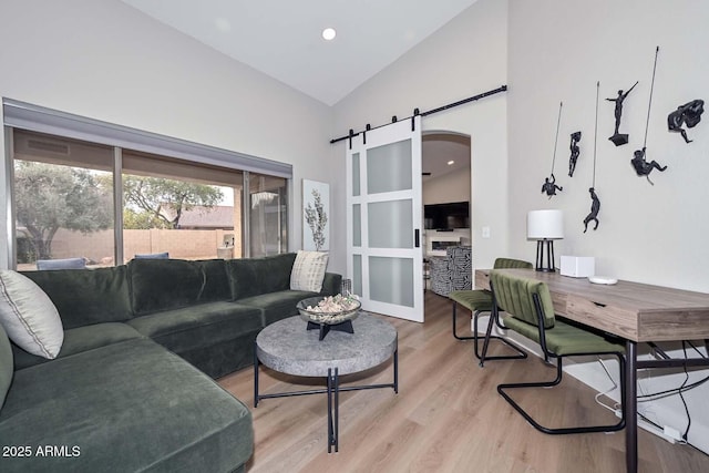 living room with a barn door, high vaulted ceiling, and light hardwood / wood-style flooring