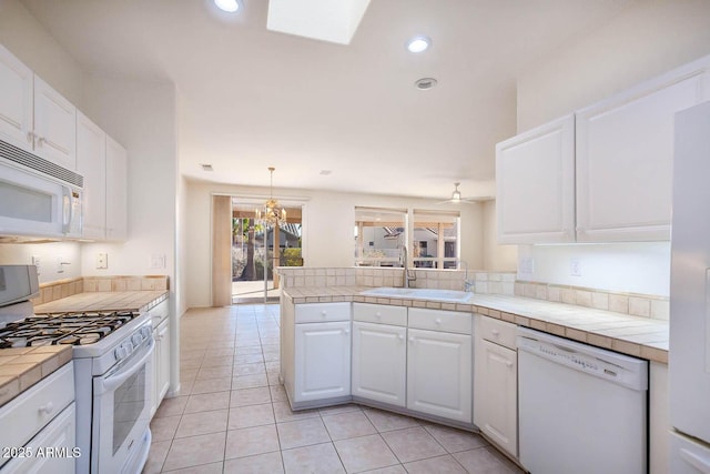 kitchen featuring white appliances, tile counters, kitchen peninsula, and white cabinets