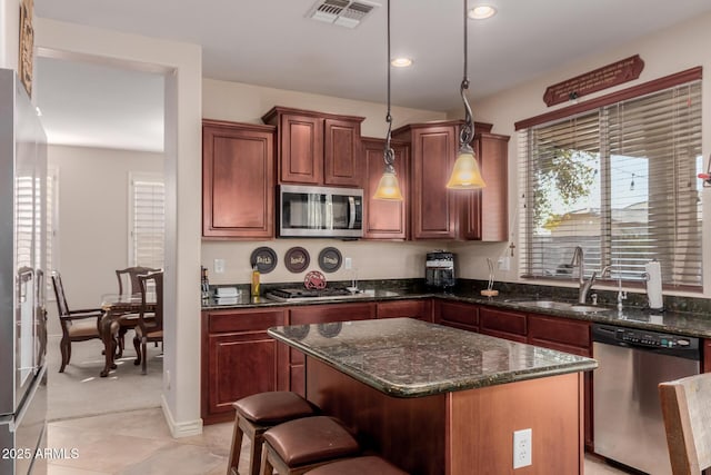 kitchen with light tile patterned floors, stainless steel appliances, hanging light fixtures, a kitchen island, and sink