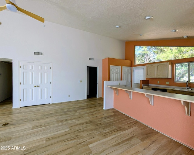 kitchen with a kitchen bar, high vaulted ceiling, light wood-type flooring, light countertops, and ceiling fan